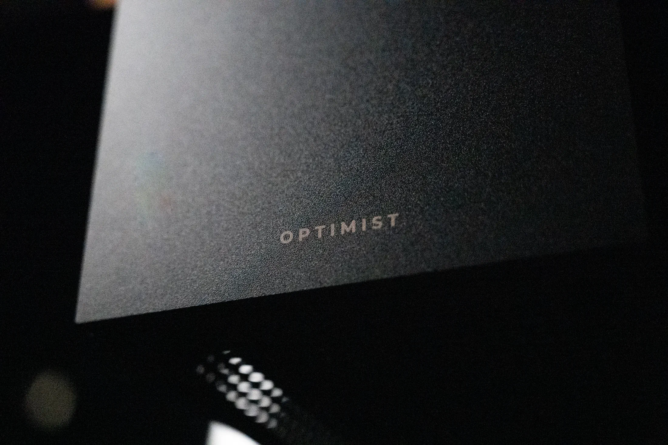 The laser-etched OPTIMIST wordmark on sandblasted black aluminum